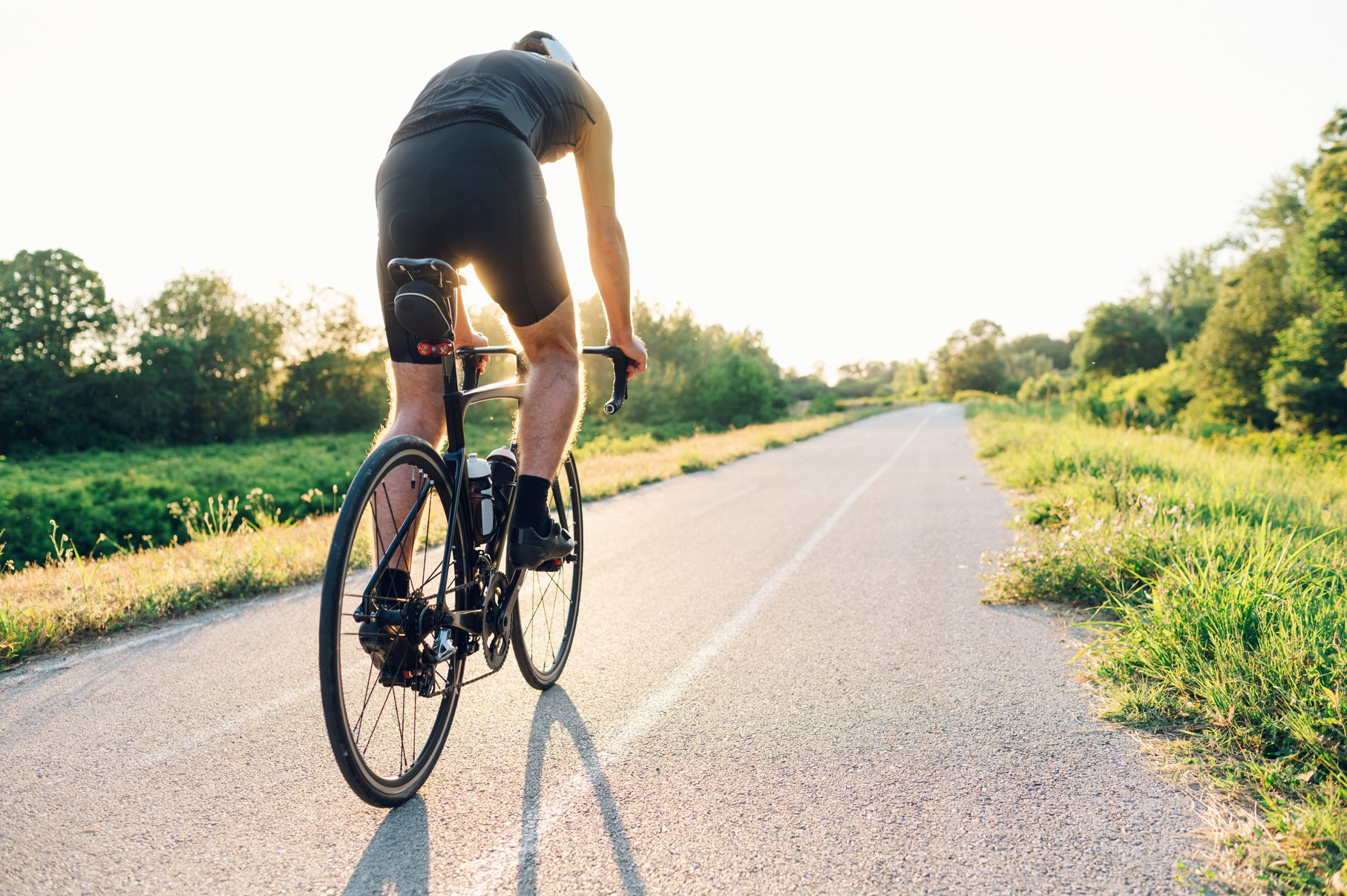 Rear view of a cycling man riding a bike outside during a sunset